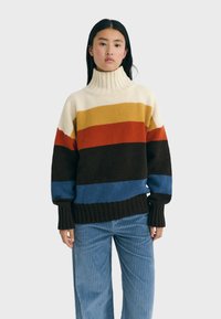 Multikleurige gebreide trui met een hoge geribde kraag. Kleuren zijn crème, geel, rood, bruin en blauw. Losse pasvorm met geribde zoom.