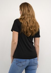 Melnas īsām piedurknēm T-kreklas ar apaļu kakla izgriezumu, apvienots ar gaiši zila džinsiem ar aizmugurējo kabatu detaļām un pieguļošu siluetu.