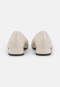 Beige läderskor med låg klack, slät yta, rund tå och minimal s�ömdetalj. Sulan har en kontrasterande svart kant.