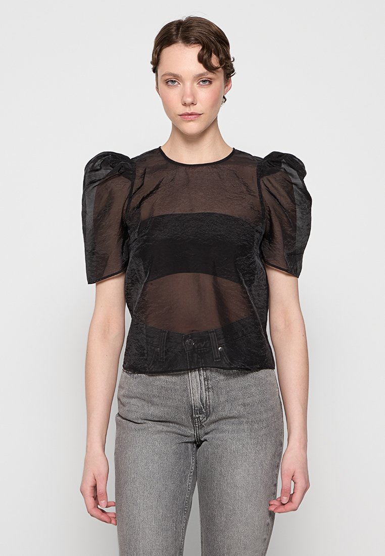 Zwarte doorzichtige top met opgezette mouwen en een iets cropped pasvorm. Het heeft een textuurstof en een kleine knoopsluiting bij de taille.