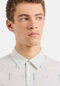 Camicia a righe di colore chiaro con colletto a bottoni, caratterizzata da piccoli motivi testuali su tutta la stoffa. Texture liscia e vestibilità aderente.