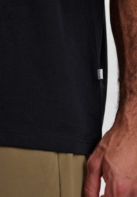 Sort bomulds T-shirt med korte ærmer, der har et side-seam label og en lige kant. Stoffet virker glat og let.