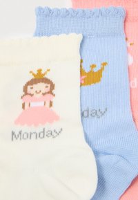 Τρία ζευγάρια παιδικών κάλτσων σε κρεμ, μπλε και ροζ. Κάθε ζευγάρι απεικονίζει μια καρτούν πριγκίπισσα και τη λέξη "Δευτέρα". Σχέδιο με κυματιστό μανίκι.