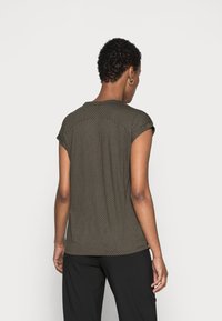 Back view of a short-sleeve, dotted pattern top in dark green with a relaxed fit. The fabric appears smooth, complemented by a rounded neckline.