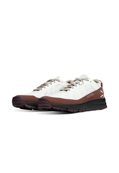 Une paire de baskets basses avec des dessus en maille blanche, des intercalaires marron, des semelles noires, des lacets beiges et des détails de logo sur les côtés et le talon.