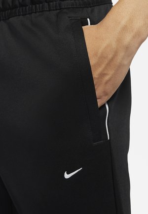 Zwarte sportbroek van gladde stof. Bevat een wit Nike-logo en een witte accent langs de zijzak. Elastische tailleband voor comfort.