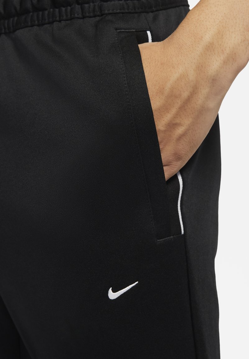 Zwarte sportbroek van gladde stof. Bevat een wit Nike-logo en een witte accent langs de zijzak. Elastische tailleband voor comfort.