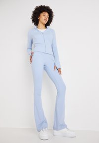 Set di activewear azzurro chiaro composto da un top con zip e colletto alto e pantaloni svasati, realizzati in tessuto elasticizzato. Scarpe da ginnastica bianche completano il look.