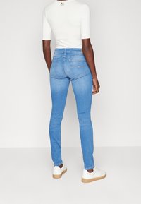 Modré skinny džíny z denimu, s vysokým pasem, zadními kapsami a jemnými švy. Kombinováno s bílými teniskami.