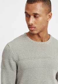 Hellgrauer Strickpullover mit rundem Ausschnitt, ausgestattet mit einem strukturierten Muster und glatten horizontalen Streifen auf der Brust und den Schultern.