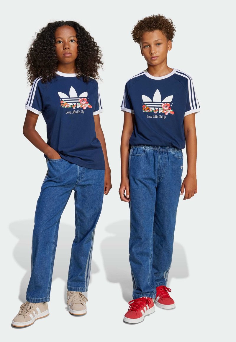 Ναυτικά T-shirts με λευκή περιχειρίδα και λουλουδάτο γραφικό; χαλαρά τζιν σε μπ�λε απόχρωση; ένας με κόκκινα αθλητικά παπούτσια, ένας με μπεζ, και οι δύο με λευκές λεπτομέρειες.