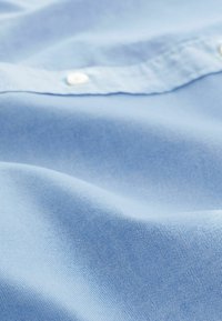 Jasnoniebieska tkanina o delikatnej fakturze i subtelnym wzorze, z białym guzikiem i gładkim wykończeniem.