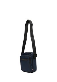 Námořnická kabelka přes rameno s černým popruhem a vyraženým logem. Hladká tkanina s horním zipem a přední kapsou na zip. Kompaktní a obdélníkový tvar.