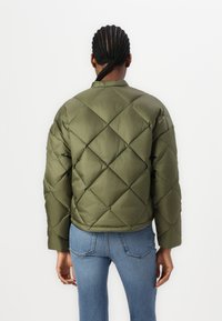 Veste matelassée en vert olive, de forme carrée avec des poignets côtelés, dotée d'un col montant et d'un motif en losanges.