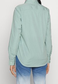 Zeleno-bílý pruhovaný dlouhý rukáv s klasickým límcem, knoflíkovými manžetami a zaobleným lemem, vyrobený z hladké tkaniny.