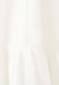 Bílá bavlněná látka s vyšívanými květinovými vzory, s texturovaným povrchem a nařaseným, volánkovým lemem.