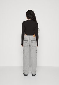 Cămașă neagră cu mâneci lungi și detaliu decupat la spate, asortată cu pantaloni cargo lejeri, de culoare gri deschis, cu multiple buzunare.