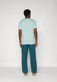 Lys grøn kortærmet t-shirt med rund hals, parret med tealfarvede breddebukser og sneakers. Har et lille hvidt logo på ryggen.
