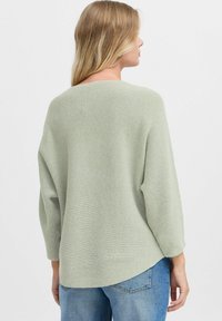 Maglione a coste di un verde chiaro, con vestibilità rilassata, maniche larghe e orlo arrotondato, abbinato a jeans blu a vita alta.