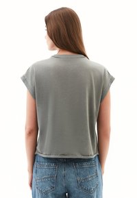 Grå, kortærmet top med en afslappet pasform og rund halsudskæring, lavet af blødt materiale, set fra bagsiden. Kombineret med højtaljede jeans.