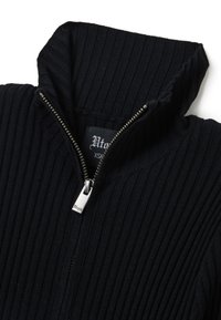 Suéter negro de canalé con cierre de cremallera y cuello alto. Cuenta con una cremallera plateada y una etiqueta en el interior. El material parece texturizado y ligero.