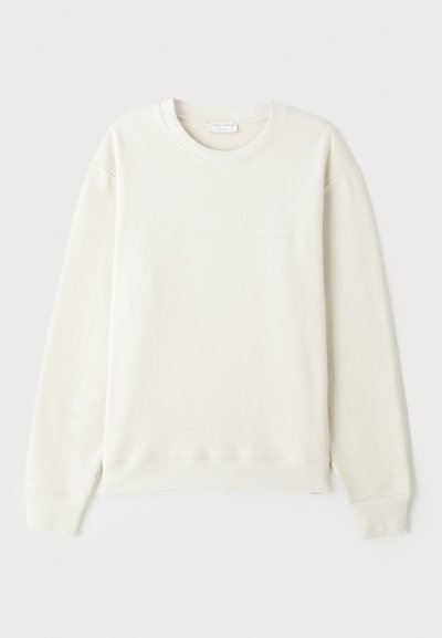 Lys beige hettegenser, bomullsmateriale, rund halslinning, lange ermer, ribbestrikkede mansjetter og hem, minimalistisk logo på brystet, glatt tekstur.