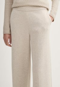 Beiga vida byxor gjorda av mjukt tyg, med en slät yta och sidofickor. Midjan är enkel och oanvänd.