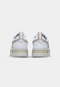 Sneakers Puma bianchi e beige viste da dietro con il logo Puma dorato e un'etichetta per il richiamo su uno sfondo bianco semplice.