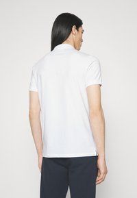 Hvit kortermet polo skjorte med klassisk krage og sideåpninger. Glatt tekstur, tettsittende snitt og minimalistisk design.