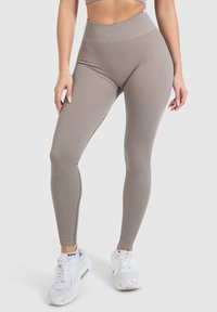 Geribbelde high-waisted leggings in licht taupe, met een naadloos ontwerp en rekbare stof. In combinatie met witte sportschoenen.