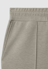 Pantaloni jogger gri din material textil, cu un tiv elastic la talie, buzunare laterale și o textură moale cu detalii discrete de cusătură.