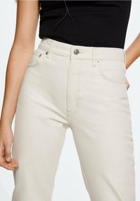 Jean taille haute beige en denim, doté d'une fermeture à bouton à l'avant, de deux poches avant et de détails de couture subtils.