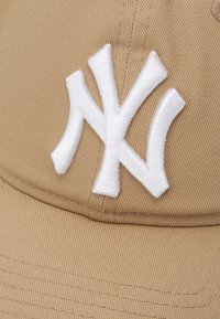 Khaki színű baseball sapka fehér hímzett "NY" logóval; bordázott textúrával; ívelt karimával; hátul állítható pánttal.