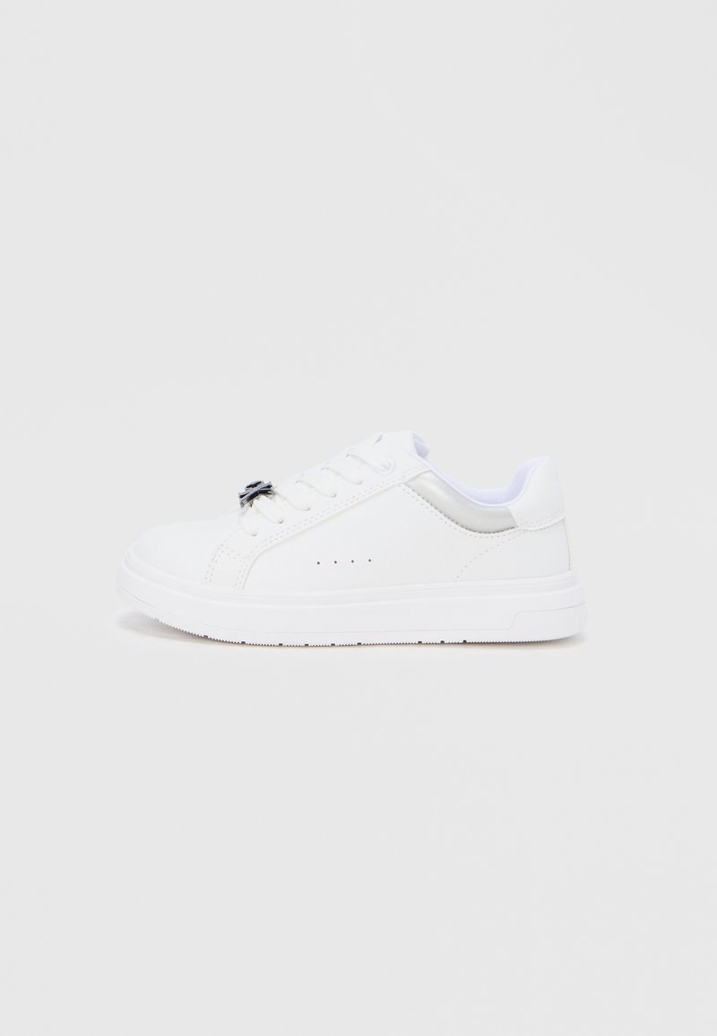 Άσπρο χαμηλό αθλητικό παπούτσι με κορδόνια στο μπροστινό μέρος, ασημί λεπτομέρεια στη φτέρνα και μικρές οπές αερισμού στη πλευρά, πάνω σε απλό φόντο.