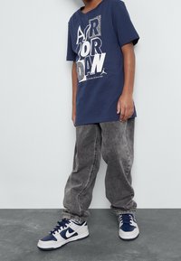 Námořnická modrá bavlněná tričková s odvážným bílým grafickým nápisem "AIR JORDAN", doplněná šedými volnými džíny a námořnicko-bílými teniskami Nike.