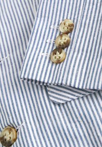 Tissu à rayures bleues et blanches avec un poignet boutonné comportant trois boutons ronds beiges et des surpiqûres visibles sur l'ourlet.