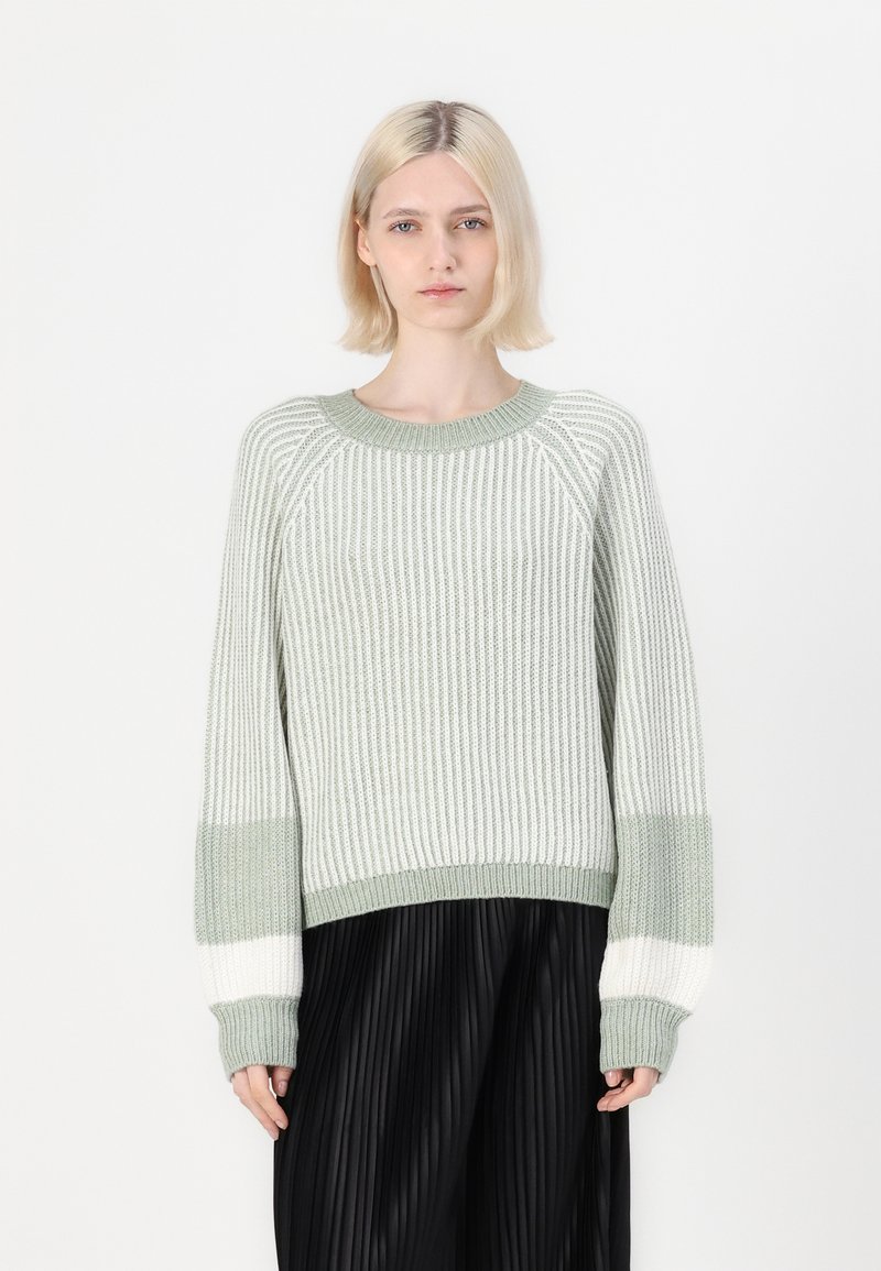 Lichtgroene gebreide trui met gestreept patroon, geribbelde textuur en oversized pasvorm; heeft contrasterende witte en donkere mouwen.