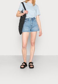 Camiseta azul claro, pantalones cortos de mezclilla de tiro alto y desgastados, bolso tote acolchado negro y sandalias negras con correas ajustables.