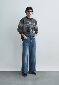Knitted sweater with dark blue, gray, and cream horizontal stripes, paired with wide-leg blue denim jeans and black shoes.