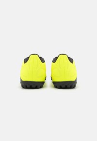 Zapatillas deportivas de color amarillo brillante con una textura suave, detalles en negro y suelas de goma que presentan púas distintas para mayor tracción.