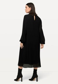 Mekko, jossa on mustat laskostukset, pitkät puffihihat ja takana avainaukko. Yhdistetty mustiin nilkkureihin, joissa on terävä kärki ja korkea korko.