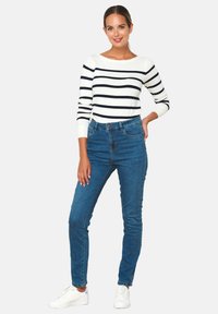 Svītrains garām piedurknēm augšdaļa baltā un tumši zilā krāsā, apvienota ar zilām augstām džinsu biksēm un baltām sporta kurpēm. Ikdienas izskats, gluda tekstūra un tīra dizaina estētika.