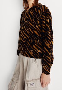 Pull-over en velours avec un motif à rayures de tigre noir et or, doté d'une coupe décontractée et de manches longues. Associé à un pantalon cargo beige clair.