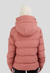 Chaqueta acolchada rosa con capucha, que presenta un diseño acolchado y puños elásticos. Se lleva un gorro de textura crema en la cabeza.