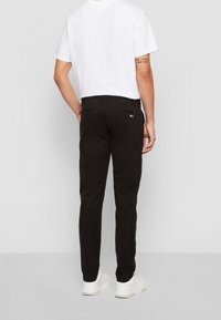 Černé bavlněné kalhoty slim fit se bočními kapsami, s malým logem na zadní kapse, v kombinaci s jednoduchým bílým tričkem a bílými botami.