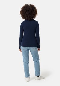 Granatowa bluzka z długim rękawem o dopasowanym kroju, zestawiona z jasnoniebieskimi dżinsami i białymi trampkami. Tekstura wydaje się gładka i miękka.