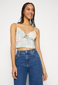 Top cropped floral em azul claro com acentos em rosa, apresentando um fecho frontal com laço e alças finas, combinado com jeans azuis de cintura alta.
