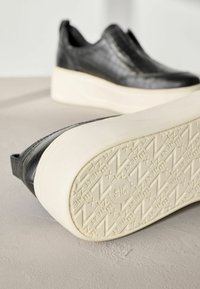 Schwarze Slipper mit einer strukturierten Oberseite und Plattformsohle. Die Sohle ist cremefarben und hat ein gemustertes Profil für besseren Halt.