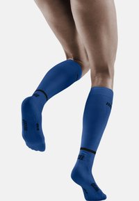 Blaue Kompressionsstrümpfe mit strukturiertem Design, schwarzen Akzenten und Logo. Bieten knielangen Schutz und eine enge Passform für Unterstützung.