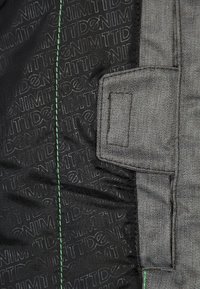 Szara denimu z teksturowanym wzorem logo. Posiada zielone przeszycia i detal kieszeni z jednej strony. Funkcjonalny i trwały design.